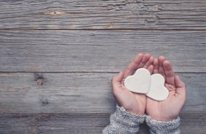 Woman holding two white love hearts. A woman is holding them in her hands. There is a rustic wood table underneath her hands. Valentines day or anniversary concept. Copy space.